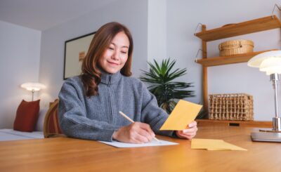 Portrait image of a young woman writing on a letter and envelopes