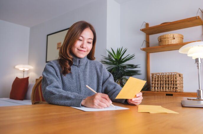 Portrait image of a young woman writing on a letter and envelopes