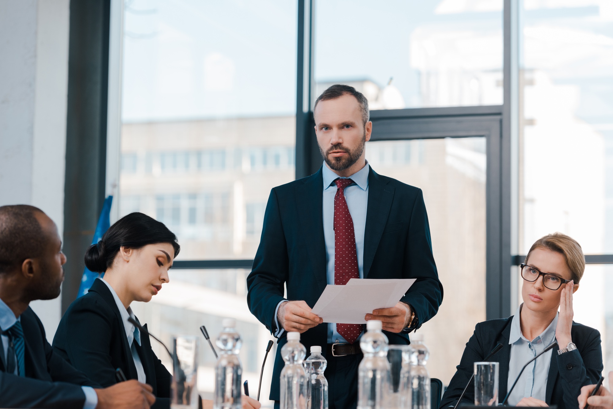 selective focus of bearded businessman holding papers near multicultural diplomats and bottles with