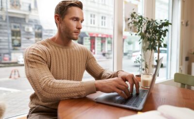 Serious looking cafe owner, handsome man working on laptop, visitor in coffee shop sending an email