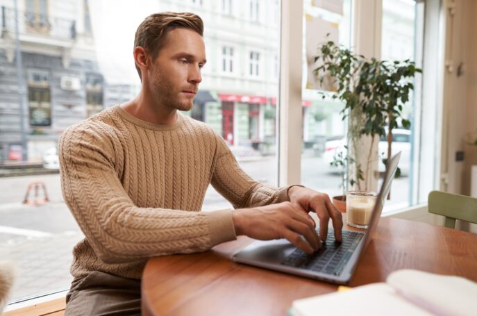 Serious looking cafe owner, handsome man working on laptop, visitor in coffee shop sending an email