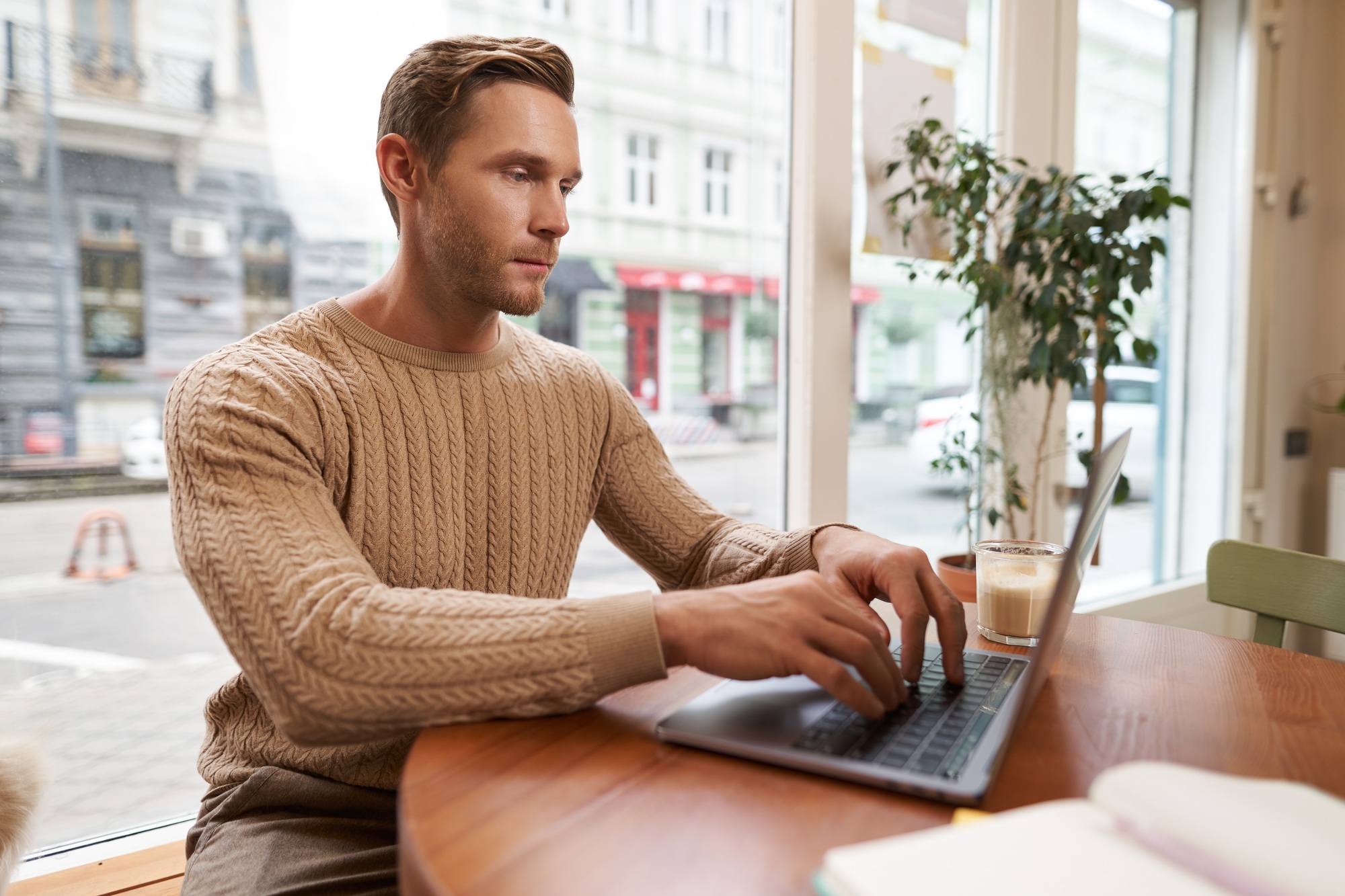 Serious looking cafe owner, handsome man working on laptop, visitor in coffee shop sending an email