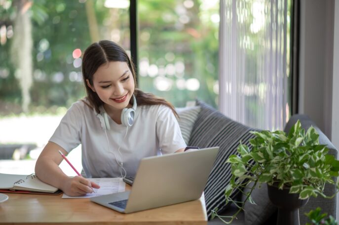 Asian woman is studying online and taking notes on the home.